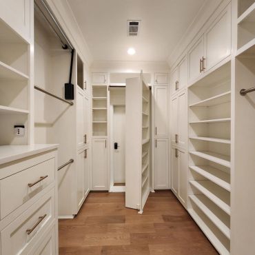 Modern white walk-in closet with wooden floor.