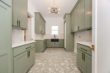 Modern kitchen with green cabinets and patterned floor tiles.