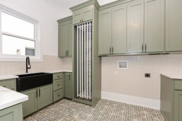 Modern laundry room with green cabinets and patterned floor.