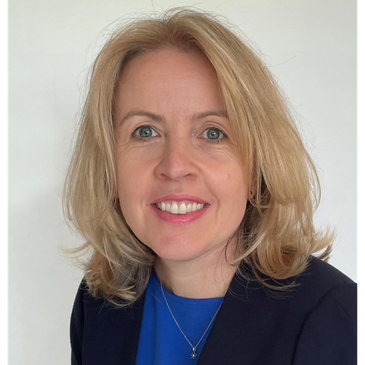 Smiling woman with blonde hair wearing a blue top and black blazer.
