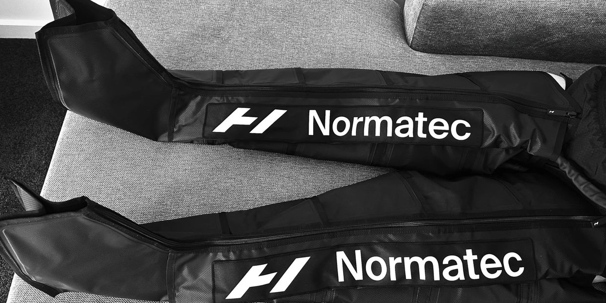 Pair of black Normatec compression leg sleeves on a grey surface.