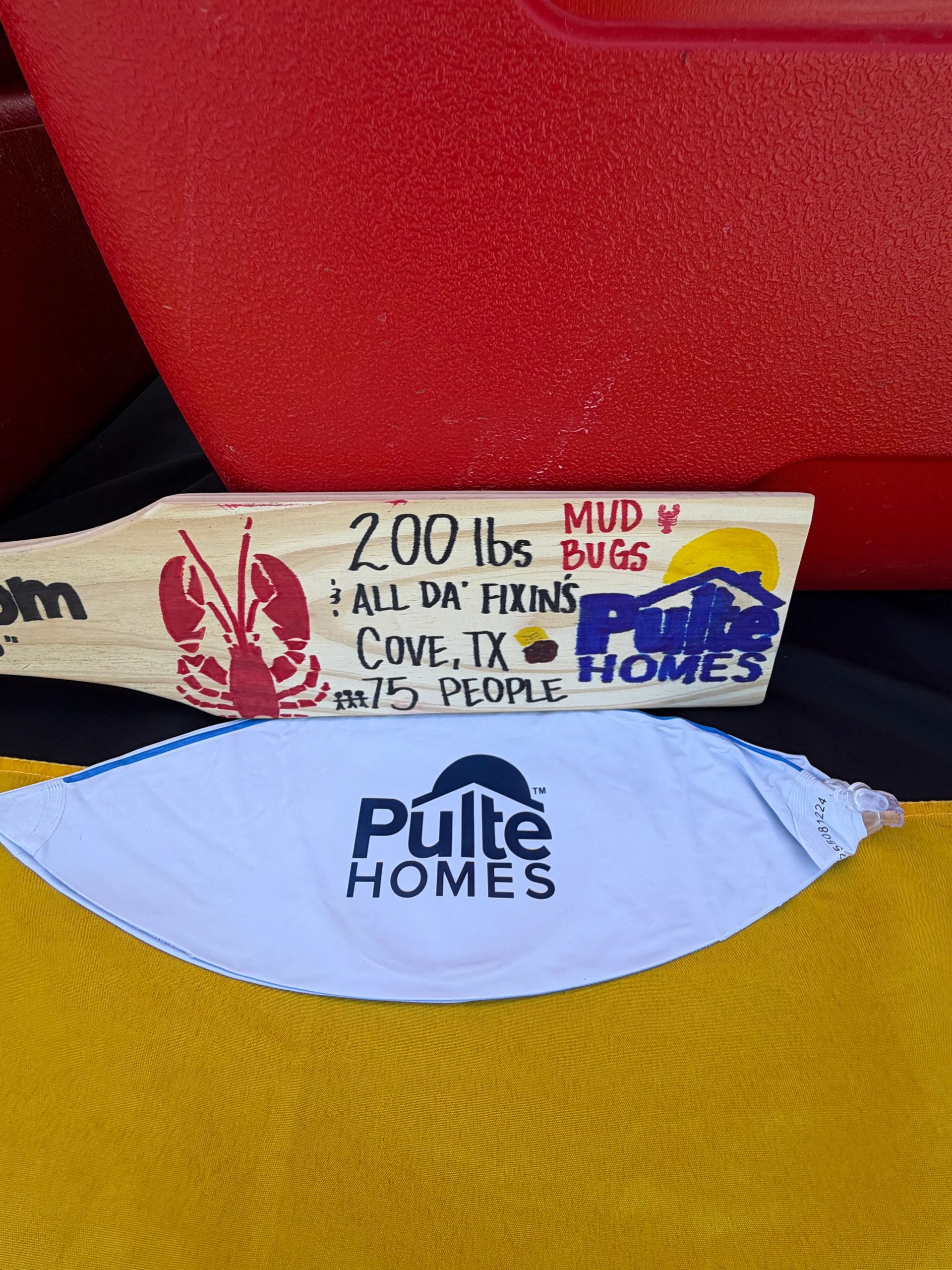Decorated wooden paddle and Pulte Homes cloth on yellow and red background.