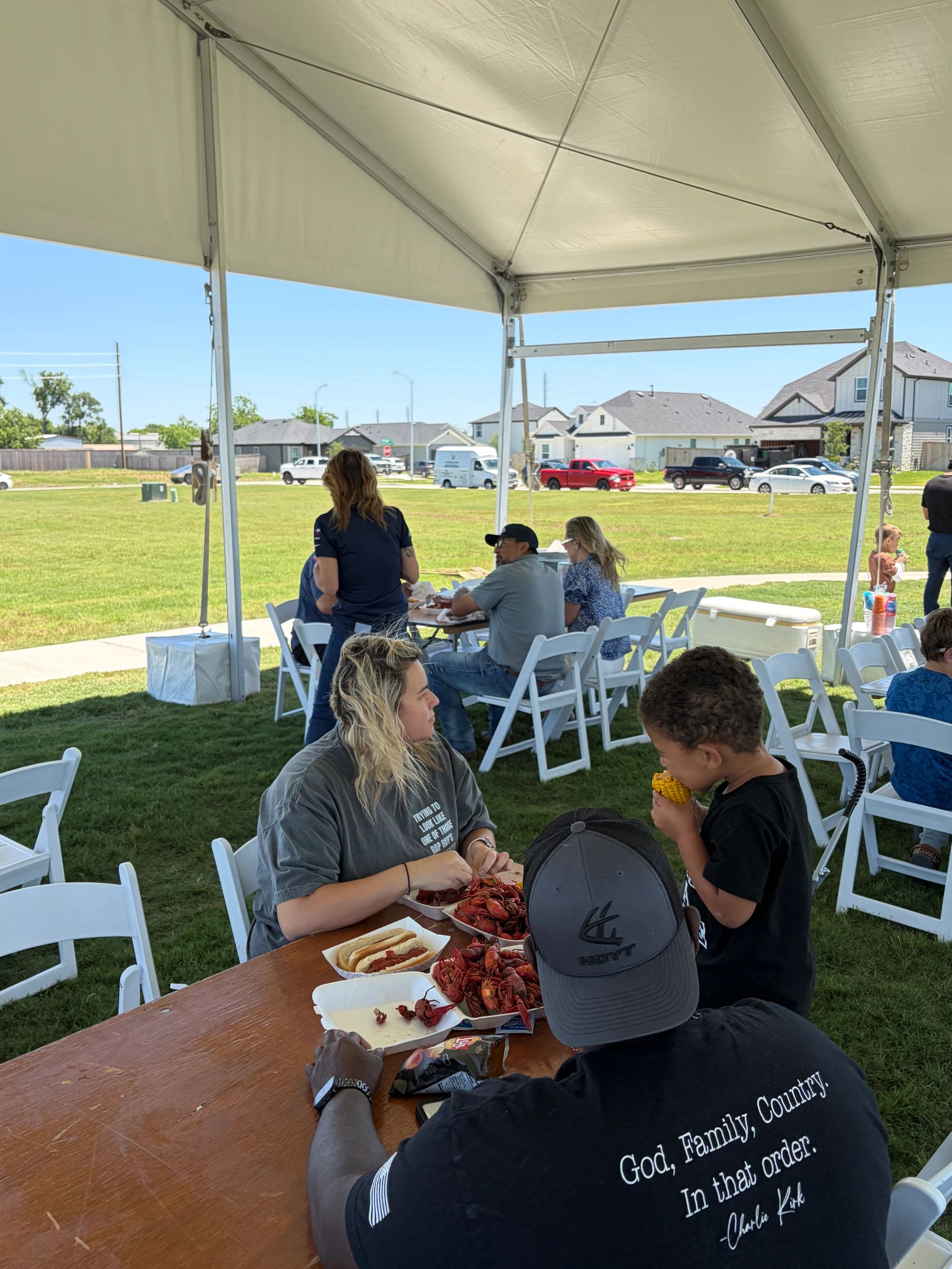 People enjoying a crawfish boil under a large outdoor tent on a sunny day.