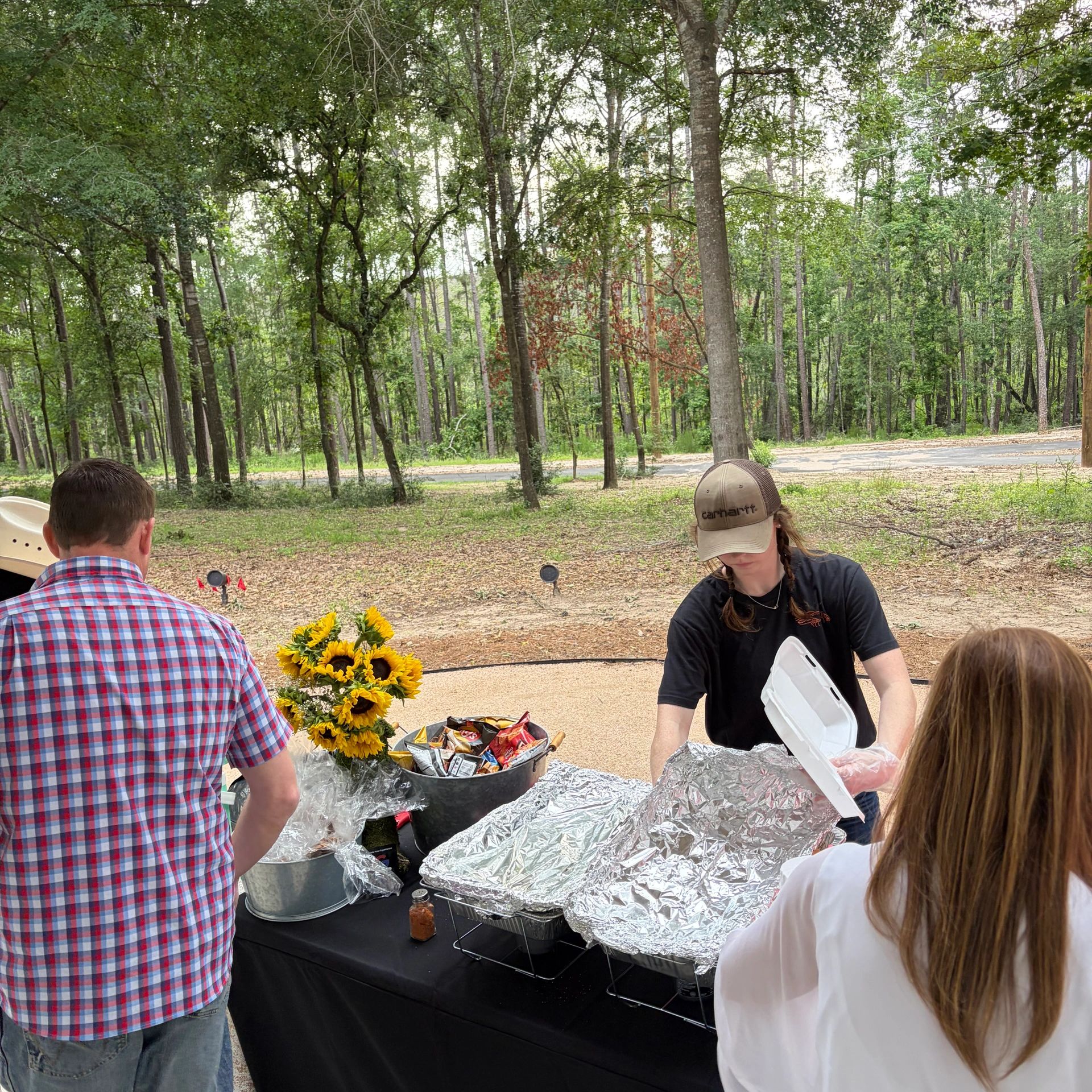 Outdoor food serving with sunflowers and people in casual attire.