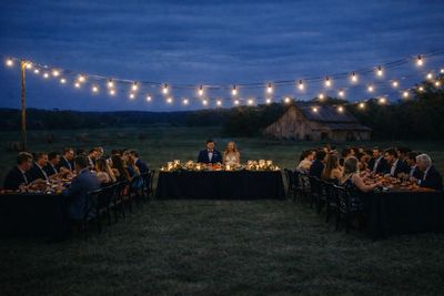Outdoor evening wedding reception with string lights and guests seated at tables.