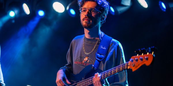 Musician playing electric bass guitar under blue stage lights.