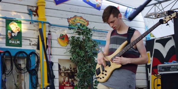 Young man playing bass guitar in a cozy, decorated indoor space.