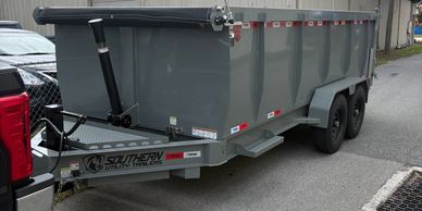 A gray utility trailer hitched to a vehicle on a paved road under a cloudy sky.
