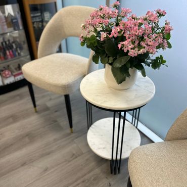 Elegant pink flowers in a white pot on a marble side table between beige chairs.
