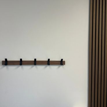 Minimalist wall-mounted coat rack with black hooks and wood paneling.