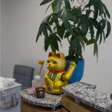 Golden Maneki-neko cat figurine on a marble countertop with plants and candles.