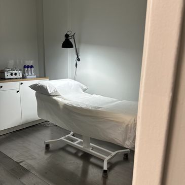 Minimalist medical or spa treatment room with a covered bed and lamp.