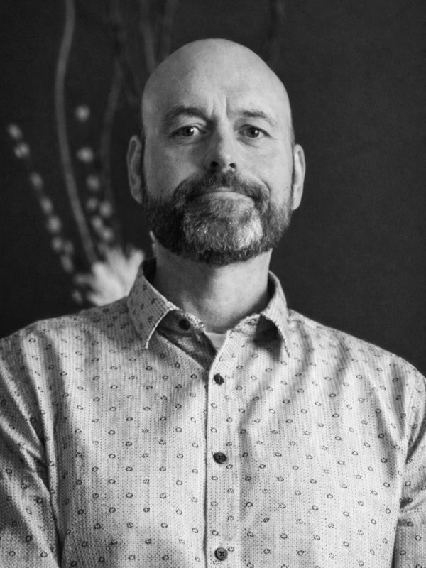 Portrait of a bald man with a beard in a patterned shirt.
