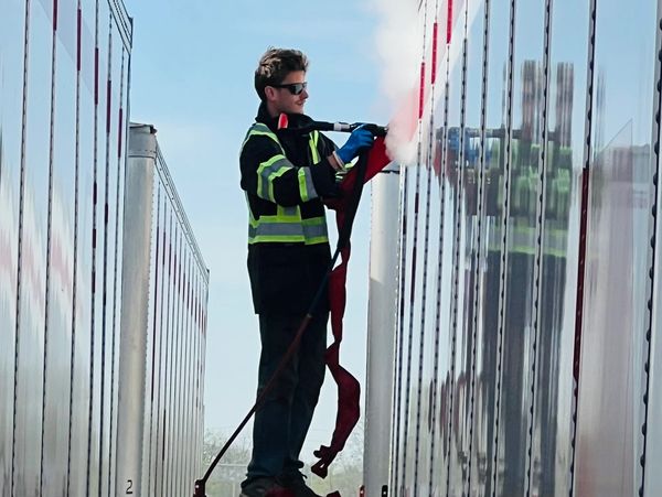Firefighter in safety gear using a fire hose between trailers.