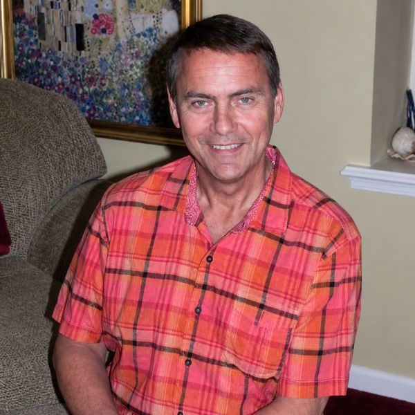 Man smiling in red plaid shirt sitting indoors.