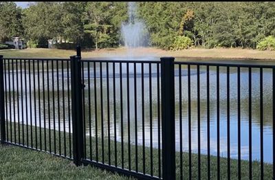Black metal fence around a pond with a water fountain.