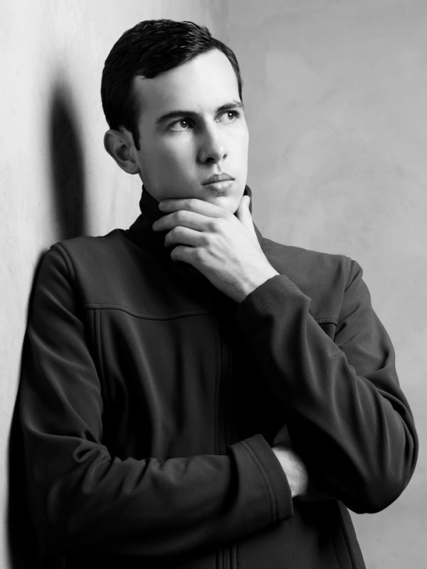 Thoughtful young man in black jacket posing against a wall.