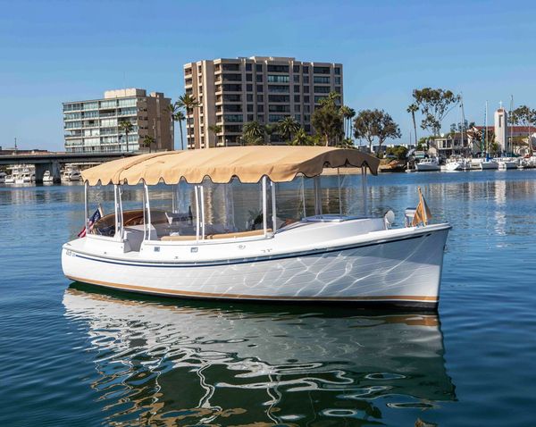 White boat with tan canopy floating on calm water near city.
