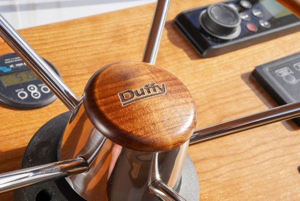 Close-up of a wooden boat steering wheel with 'Duffy' engraved.