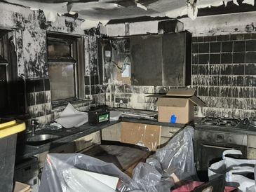 Fire-damaged kitchen with soot-covered walls and cabinets.