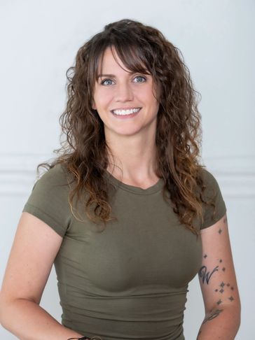 Smiling woman with curly hair and tattoos wearing a green t-shirt.