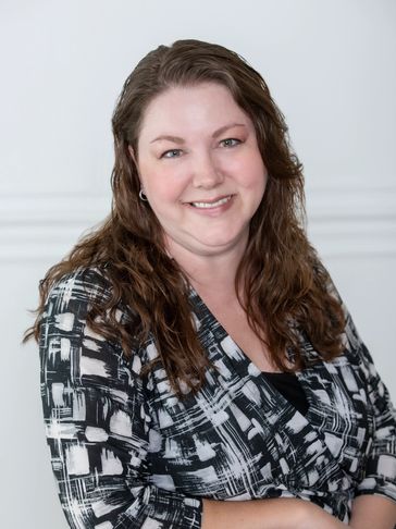 Smiling woman with long brown hair wearing a black and white patterned blouse.