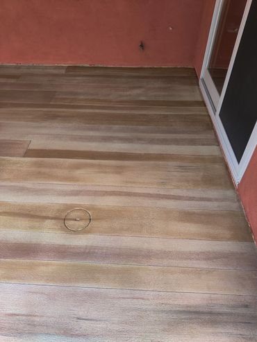 A wooden deck with a circular access panel near a red wall and a sliding door.