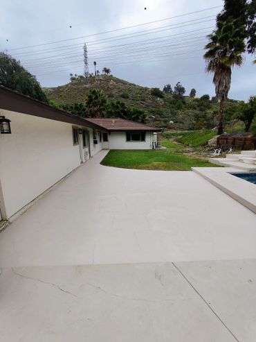 Backyard patio with green lawn and hill view under cloudy sky.