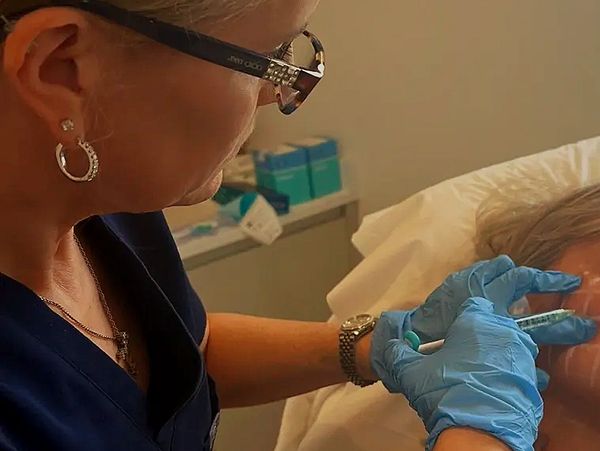 A medical professional administers an injection to a patient's face.