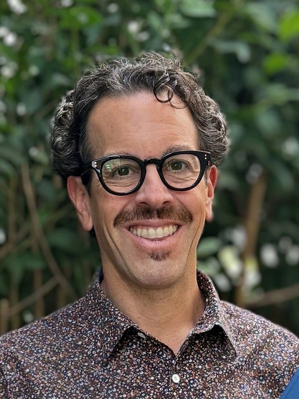 Man with glasses smiling outdoors.
