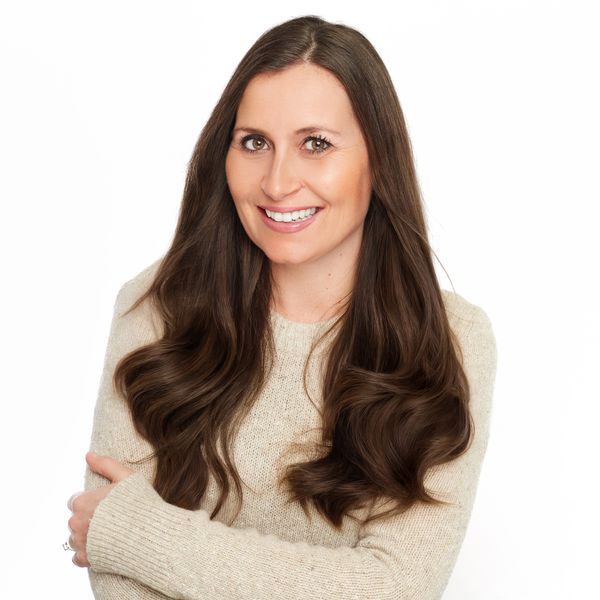 Smiling woman with long brown hair wearing a beige sweater against a white background.