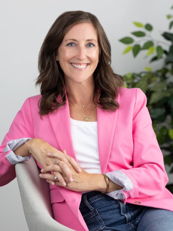 Smiling woman in pink blazer sitting in a chair.