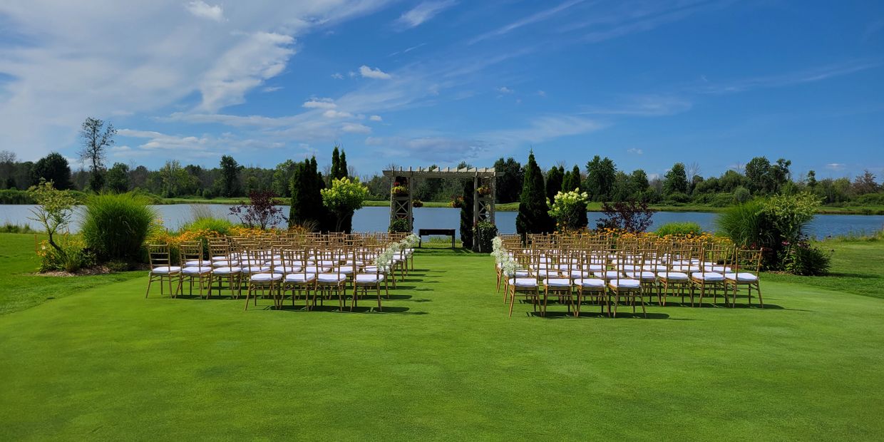 Outdoor wedding setup with chairs facing a decorative arch near a lake.