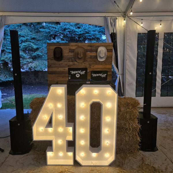 Illuminated '40' sign at a rustic outdoor event setup with hay bales and hats.