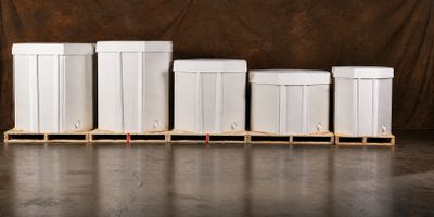 Five white storage bins of different sizes on wooden pallets against a brown backdrop.