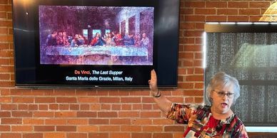 A woman giving a presentation on Da Vinci's The Last Supper in front of a brick wall.