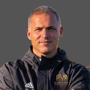 Man wearing a black jacket with a sports academy logo on a gray background.