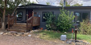 Gray house with wooden porch and green bushes.