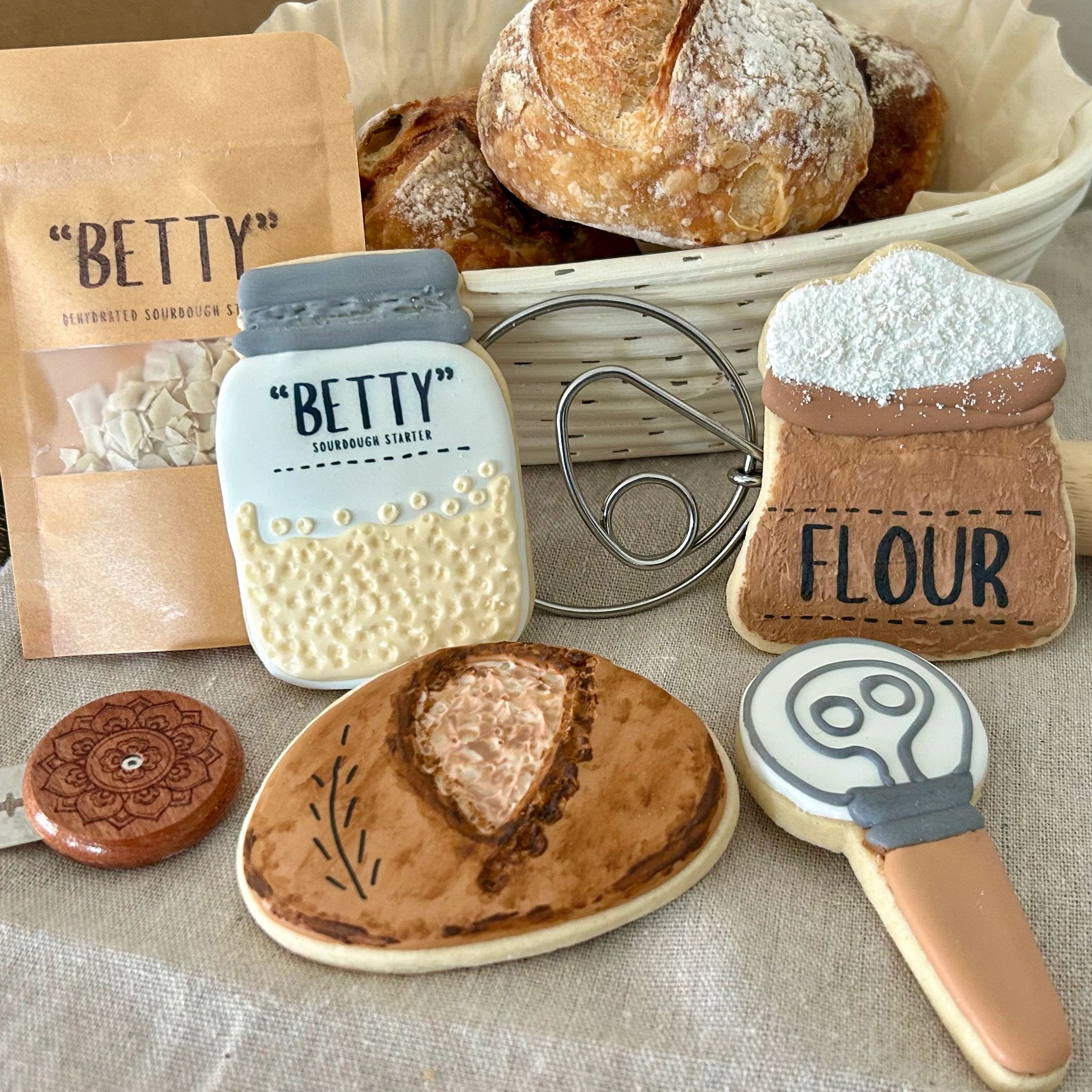 Decorative cookies shaped like baking items and a hat with sourdough bread in the background.
