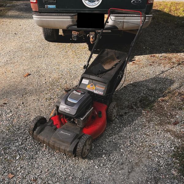 Red and black Snapper lawn mower on gravel driveway in front of a truck.