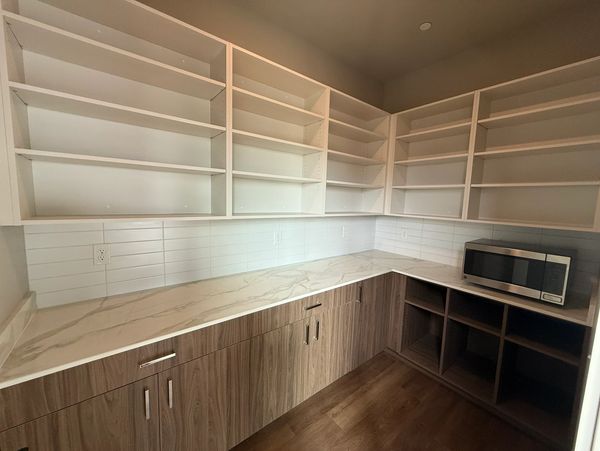 Empty modern kitchen pantry with shelves and microwave.