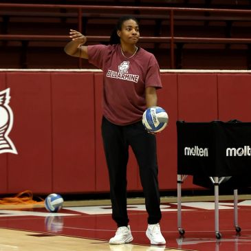 Woman holding a volleyball and pointing on a court.