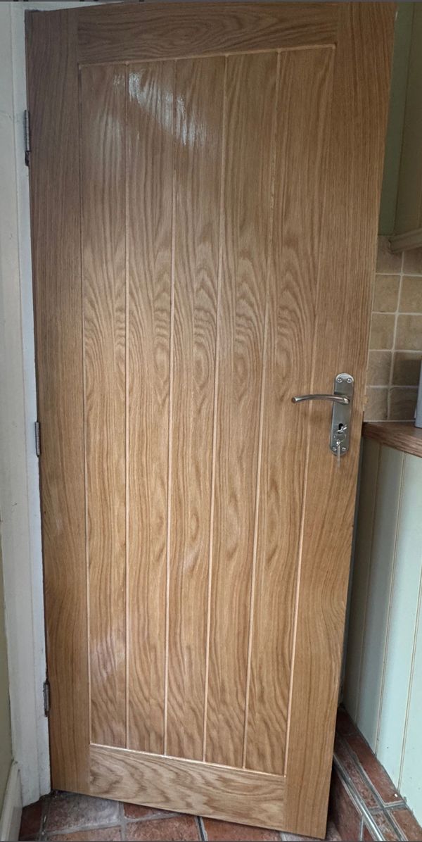 Wooden door with metal handle in a tiled room corner.
