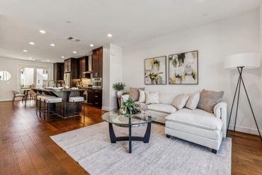 Bright open living room with white sofa and modern kitchen in background.