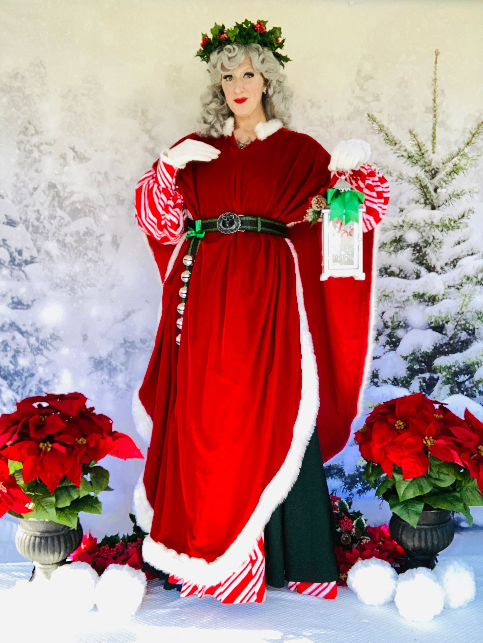 Mrs. Claus holds a lantern while dressed in full formal red velvet, white fur, and holiday garland.