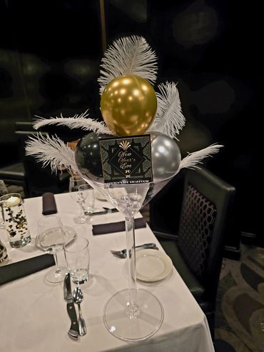 New Year's Eve table centerpiece with balloons and feathers in a tall glass.