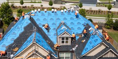 Workers installing shingles on a large roof.