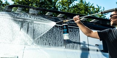 Man washing a van with a high-pressure water hose outdoors.