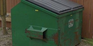 A green metal dumpster with rust spots on a concrete ground.
