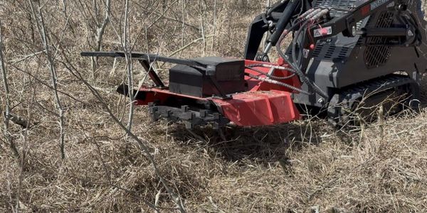 A tracked brush cutter clearing dry brush in a field.